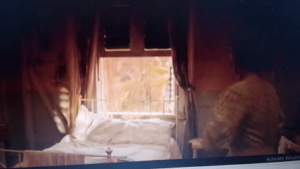 Woman in dress stands bedside in dimly lit room