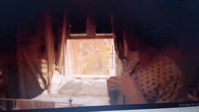 Woman in dress stands bedside in dimly lit room