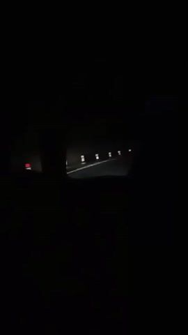 The video shows a dark, nighttime view from inside a vehicle. The road ahead is dimly lit by intermittent reflective markers and possibly distant headlights. The interior of the vehicle is mostly blacked out, with the exception of a faint glow from the dashboard or a device within the car. The overall impression is one of travel through a dark, unlit area.
