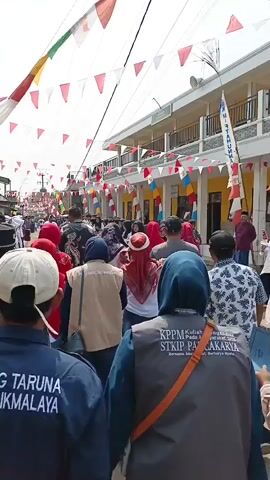A group of people are walking down a street. They are decorated with flags and banners. The people are wearing a variety of clothing. Some of the people are wearing uniforms. The street is lined with buildings. The buildings are decorated with flags and banners. The sky is cloudy.