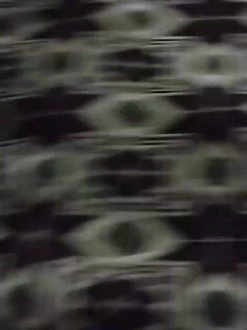 The video shows a close-up of a patterned fabric. The pattern consists of repeating geometric shapes in black, white, and a darker shade, possibly purple. The camera moves slightly, causing the image to blur intermittently. There is muffled speech audible in the background.