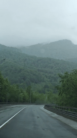 Cars navigate wet mountain road in rainy Kepsha, Russia