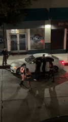 Group gathers around white car on Los Angeles street