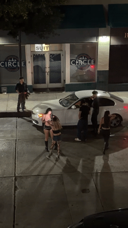 Group gathers around white car on Los Angeles street