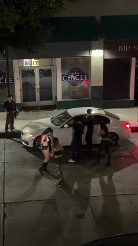 Group gathers around white car on Los Angeles street