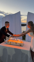 Outdoor wedding reception with cake, fireworks, and sparklers at dusk