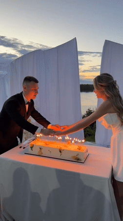 Outdoor wedding reception with cake, fireworks, and sparklers at dusk