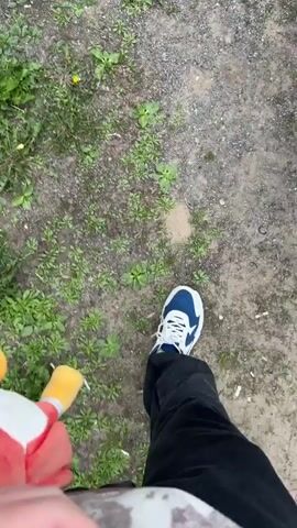 The video shows a person walking on a gravel path next to some grass, holding a Red Angry Bird plush toy. The person is wearing blue and white sneakers and black pants. The video ends as the person approaches a white car and looks into the driver's side window, revealing the steering wheel and dashboard.