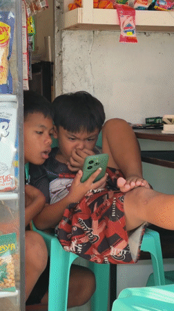 Boys share smartphone in Philippine corner store