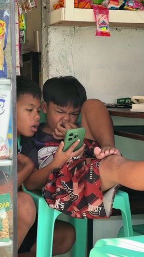 Boys share smartphone in Philippine corner store
