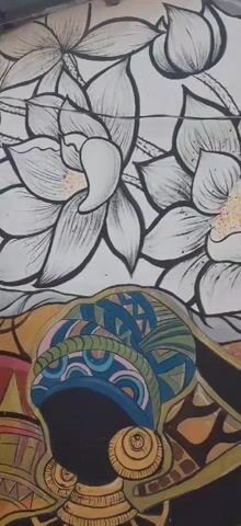 The video shows a section of a mural on an exterior wall. The mural features several distinct elements including large white flowers with black outlines and yellow centers, an eye within a triangle, a stylized depiction of a woman's face in profile with flowing hair, decorative lanterns, and a man's face with his eyes closed, wearing jewelry. The mural is colorful and appears to be in good condition. The camera pans across the mural from left to right, then pans down to show the bottom portion of the mural and the surrounding environment. The environment appears to be an outdoor space with a doorway and a potted plant.