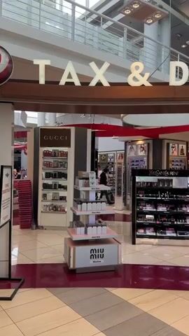 The video shows a tax and duty-free store at an airport. The store sells various luxury items such as perfume and cosmetics. It has brands like Gucci and Yves Saint Laurent displayed. There are shelves stocked with products, and some displays feature mannequins. A few employees can be seen behind the counters, and a couple of customers are browsing. The overall environment appears to be a well-lit and organized retail space within an airport terminal.