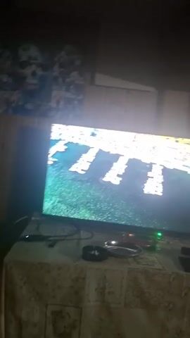 Here is a description of the video.
The video shows a television set playing a music video. The video features a woman with long red hair singing and dancing on a beach. A man is also seen playing the violin. The television is sitting on a table with various items, including a smartphone, an ashtray, and a beer bottle. The room is dimly lit.
