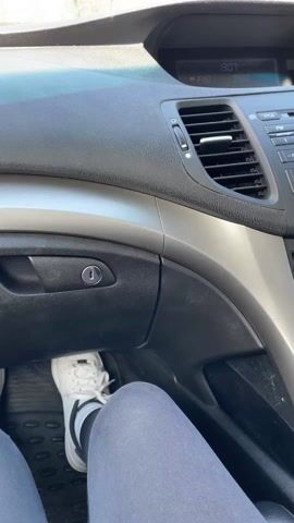 The video, shot from the interior of a car moving down a highway, captures a view through the windshield of a road bordered by trees on either side. A red car can be seen ahead on the road. The sky is blue with a few white clouds. A portion of the dashboard is visible, including the air conditioning vent and radio. A person's leg wearing a white sneaker and gray sweatpants is visible near the dashboard. Music is playing in the background.