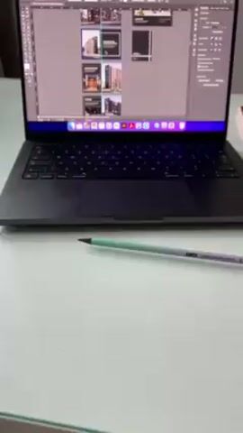 The video shows a laptop on a white table with a pen next to it. The laptop screen displays a graphic design program with multiple image previews. A window behind the laptop offers a view of a city, a body of water, and distant mountains under a cloudy sky.