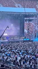 Live band performs outdoors to a packed crowd under blue and purple lights