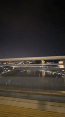 Nighttime cityscape with water reflections filmed from moving vehicle