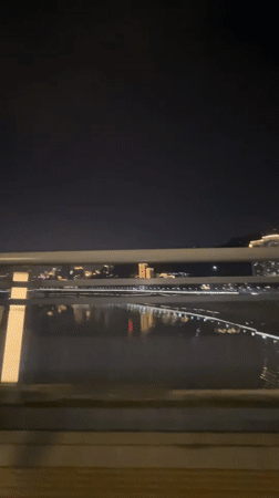 Nighttime cityscape with water reflections filmed from moving vehicle