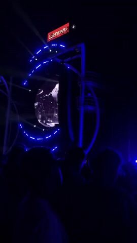 A night concert is happening. The crowd is silhouetted against the blue lights from the stage. The stage features a large disco ball and a Lenovo advertisement at the top. A DJ is visible at the stage.