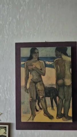 This media file contains a painting of two nude figures, likely women, standing on a beach with a dog behind them. The figure on the left is facing forward, with her hand covering her chest, and appears to be looking to the right. The figure on the right is facing away from the viewer, revealing her back and buttocks. The background depicts a blue ocean with white waves and a sandy beach. The painting's style is somewhat impressionistic, with visible brushstrokes and muted colors. The overall scene suggests a serene or perhaps contemplative moment, possibly during daylight given the illumination of the figures. There is no visible text in the painting or its frame. The painting is framed with a dark burgundy mat.