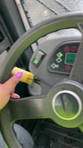 The video shows a first-person perspective from inside a vehicle, possibly a forklift, with the "Linde" logo visible on the steering wheel. It is raining heavily, obscuring the view through the windshield, which is covered in water droplets. Two other similar vehicles can be seen ahead in the rain-soaked environment, suggesting an industrial or storage yard setting. The windshield wipers are activated and partially clear the rain from the windshield. A screen, partially obscured by white paper, is attached to the windshield and displays an image that is mostly obscured.