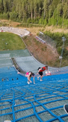 Two people climb ski jump ramp covered in netting
