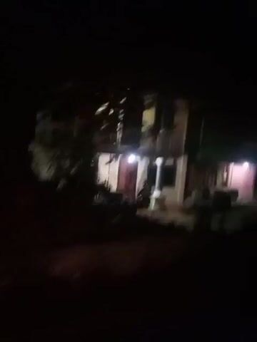 The video captures a nighttime scene. The first frame shows a two-story building with lights on, illuminating the front of the structure. The second frame shows a striped barrier, possibly a railroad crossing gate, with lights and a sign in the background, suggesting a moving vehicle. The remaining frames are dark, obscuring any details.
