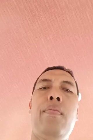 A man's face is shown from a low angle. The man is looking upwards. The background is a pink wall with a wood-grain pattern. In some frames, a wooden door frame and a door are visible. The video appears to be taken from a low perspective, possibly from the floor.