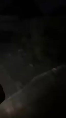 The video appears to be shot at night, possibly in an alleyway or a poorly lit outdoor area. The scene is dark, making details difficult to discern, but a building or structure is visible in the background. There is some debris or trash scattered on the ground. Brief, irregular flashes of light occur, seemingly from a handheld light source or camera flash, briefly illuminating the scene.