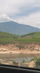 Dry riverbed and green hills captured from vehicle in Vietnam