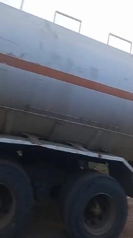 The video shows a semi-truck transporting a large, elongated object, possibly a section of an airplane fuselage, on a flatbed trailer. The object is white with a red stripe. The surrounding environment appears to be rural, with a dirt road and vegetation. The video concludes with a view of the sunrise over the landscape.