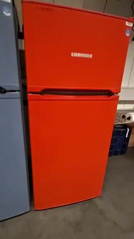 A red Liebherr refrigerator is shown. A hand reaches out and opens the refrigerator door. The interior of the refrigerator is revealed, showing shelves stocked with various items, including bottles and cartons. The door is then closed.