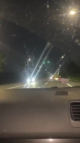 The video shows a first-person view from inside a car at night, driving on a highway. The dashboard and windshield are visible. Streetlights illuminate the road ahead, and other vehicles can be seen in the distance. There is a sign on the right side of the road. The sky is dark.