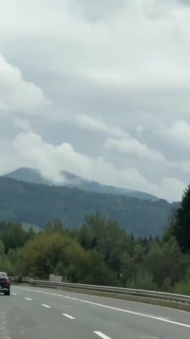 The video shows a highway with several cars on it, driving through a mountainous landscape. The sky is cloudy and the mountains are covered in trees. There is a speed limit sign visible with a speed limit of 65. The overall atmosphere is serene and peaceful.