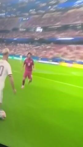 The video shows a soccer game between Portugal (POR) and Spain (ESP). The score is 0-0. A player wearing a white jersey with the number 10 on the back is in possession of the ball near the sideline. The player is facing away from the camera and appears to be dribbling the ball. Another player in a maroon jersey is defending. The field is green, and there are spectators in the stands behind the players. The game is taking place in a stadium with advertising boards visible along the sideline.