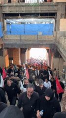 Flag-carrying crowd in black moves through arched passage in Tehran