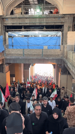 Flag-carrying crowd in black moves through arched passage in Tehran