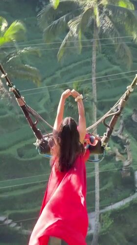 Woman in red dress swings over Tegallalang valley