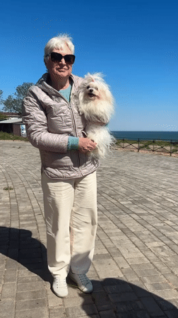 Woman walks small white dog on waterfront in Fontanka