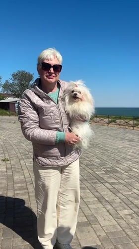 Woman walks small white dog on waterfront in Fontanka