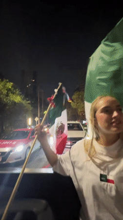 Mexican flags flying from a moving car in Mexico City at night