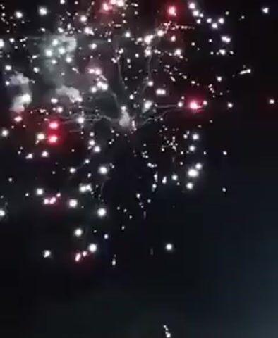 The video captures a dynamic fireworks display against a dark night sky. Multiple aerial shells explode, creating vibrant bursts of light and color. The fireworks appear in various shades, including bright red, green, white, golden, and purple, forming intricate starburst patterns and glittering effects. The explosions are accompanied by distinct crackling and booming sounds characteristic of fireworks. No people or specific location identifiers are visible within the frame, but the context indicates the event is taking place in Yambol, Bulgaria. The overall scene suggests a celebration or festive occasion.