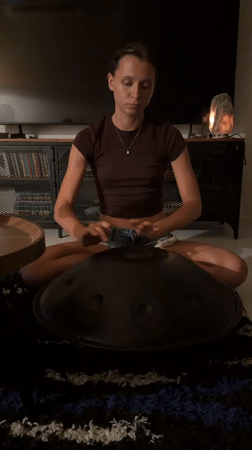 Woman plays handpan drum in dimly lit room, Chang Phueak