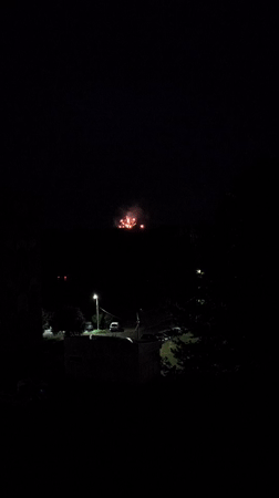 Fireworks light up the night over a lit settlement below.