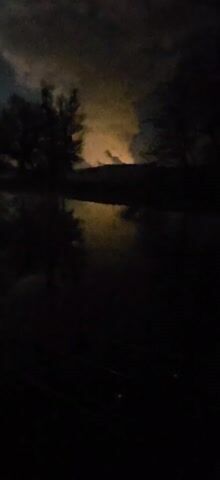 The video shows a dark scene featuring a body of water, presumably a lake or pond, with trees silhouetted against the skyline. The lighting is poor, but there is a visible reflection in the water, presumably from the moon. The video begins with a yellow glow in the background before settling on the moon as the source of light, though the scene remains quite dark. The video seems to be recorded at night.