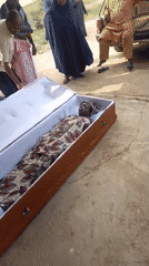 Funeral service documented with mourners gathered around casket