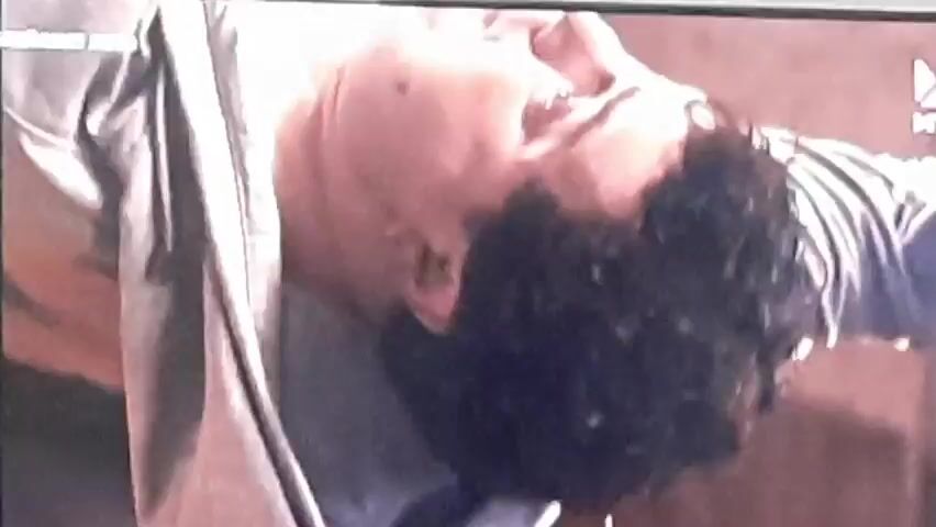 The video shows a black kitten playing with a string, then a man in a light-colored robe is shown in a suspended position, as if falling or flying. The next frame is a close-up of the man's face, appearing distressed or in pain. This is followed by a shot of what looks like a vintage kitchen appliance with a glass container, and finally, a chaotic scene with debris and what appears to be a painting or mural of a rooster being damaged.