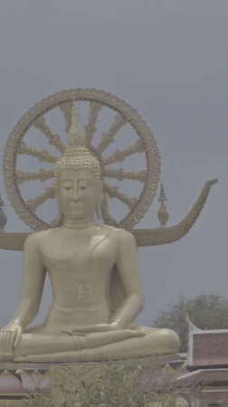 Golden Buddha statue overlooks Thai waterfront village scene