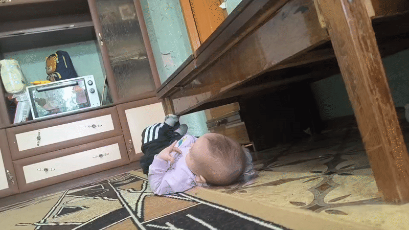 Baby reaches under table in Kostanay home
