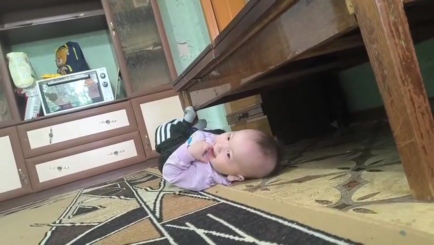 Baby reaches under table in Kostanay home